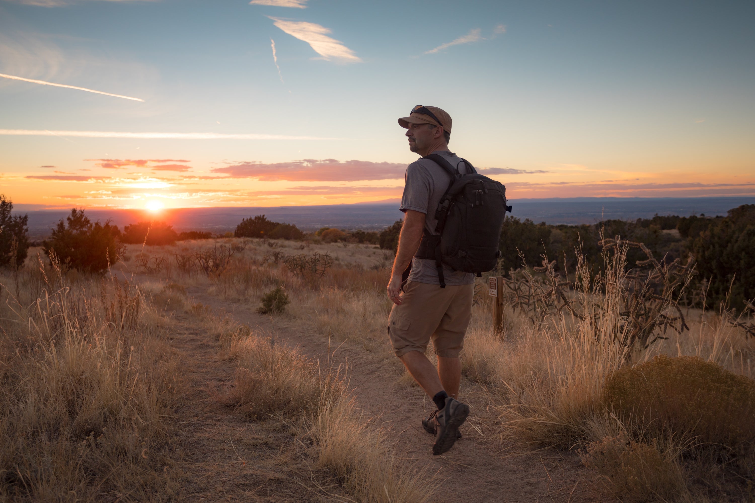 Man with a backpack walking on a trail during sunset in a desert landscape