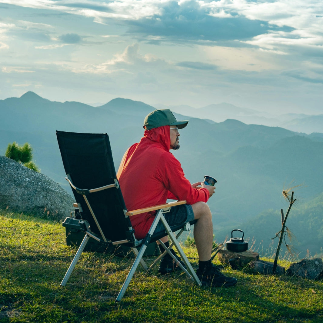 Person sitting in a folding chair on a grassy hill with mountains in the background