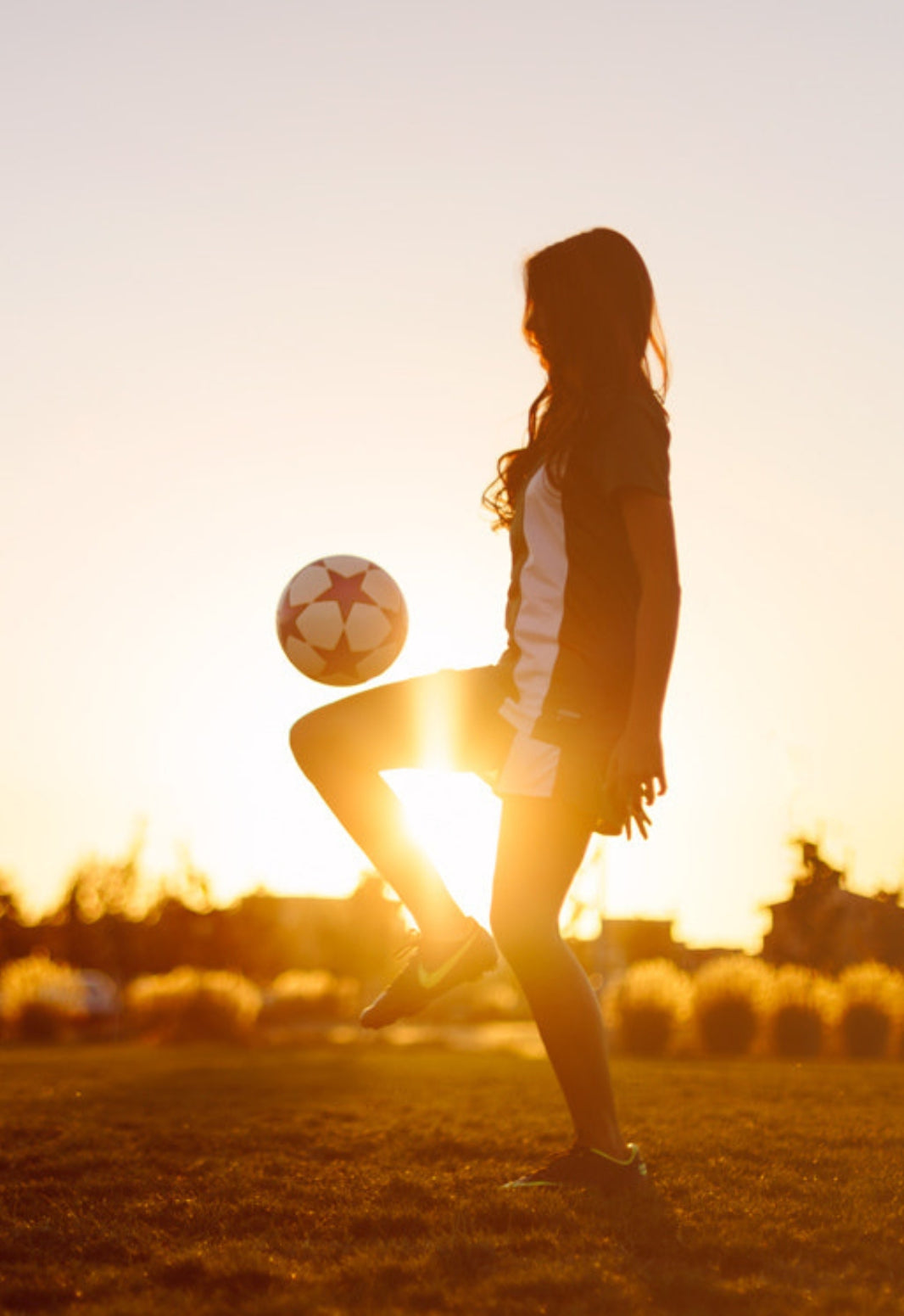 Person kicking a soccer ball on a field with a sunset background