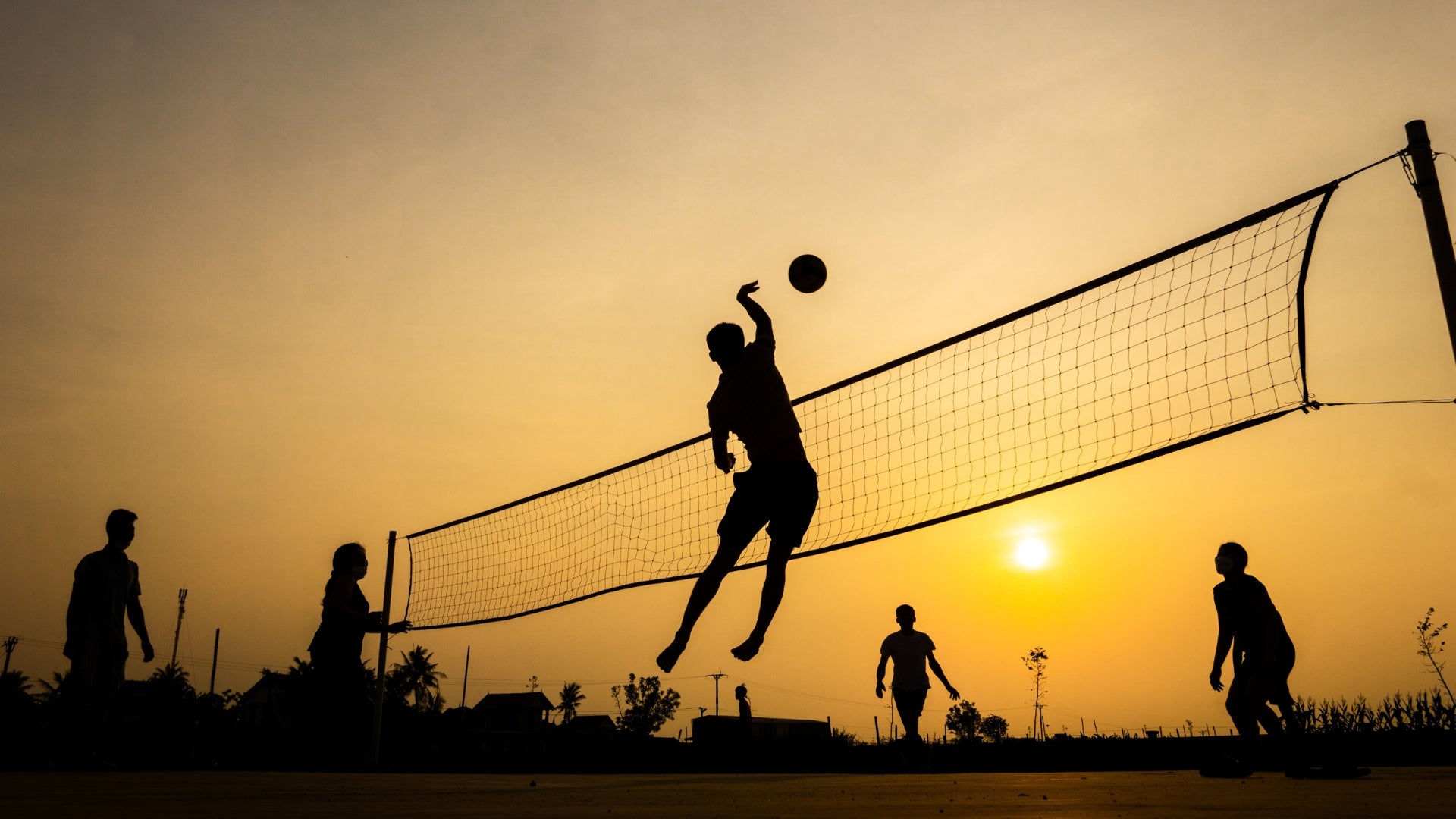 Volleyball game in progress with players silhouetted against a sunset sky.